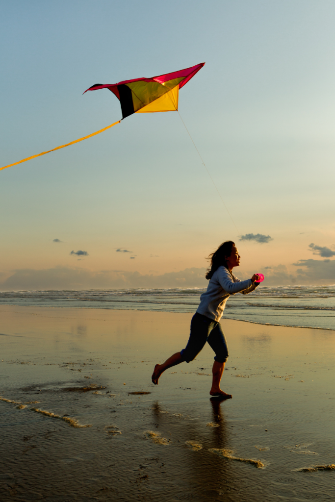 Child girl running on beach flying a kite