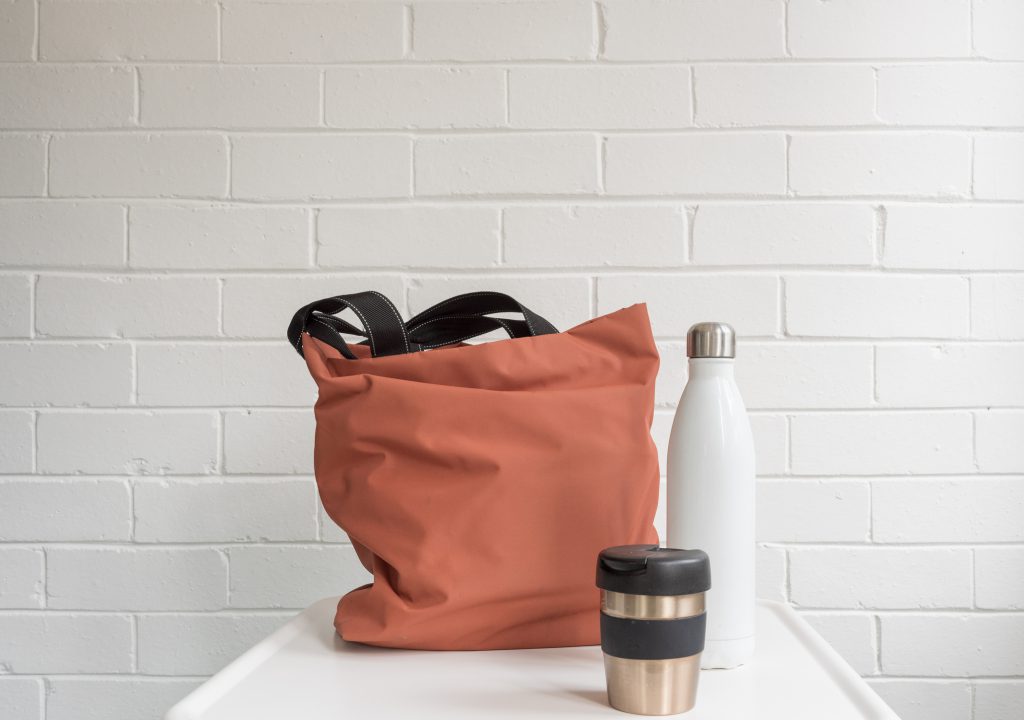 reusable coral bag, white water bottle, white brick wall in background, silver and black tumbler, white countertop