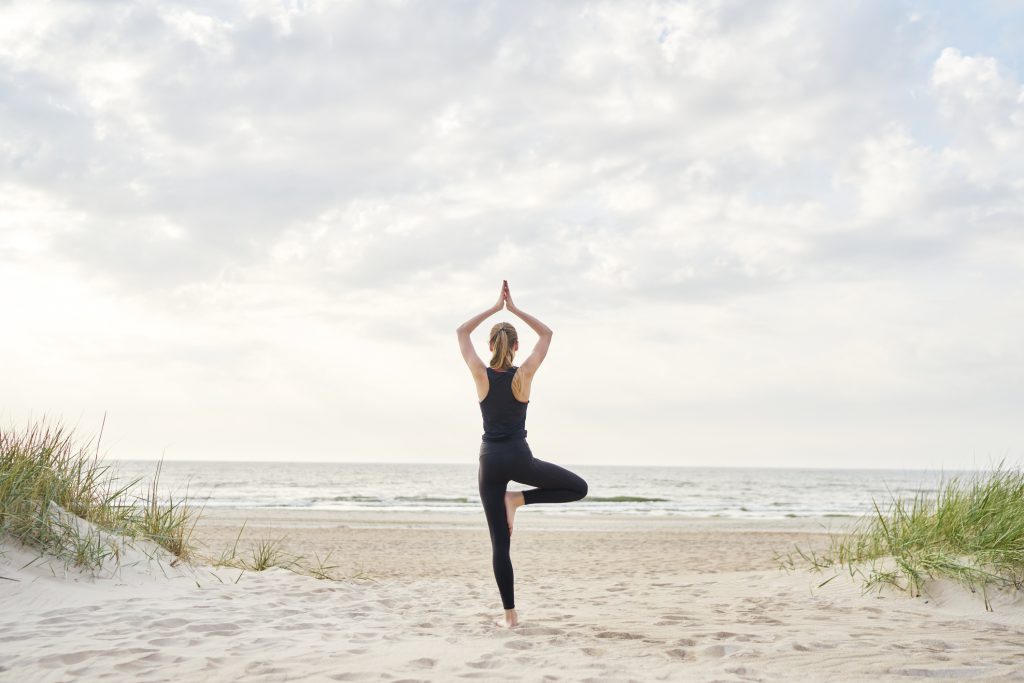 A young woman wearing gym clothes doing yoga on the beach on a sunny day.