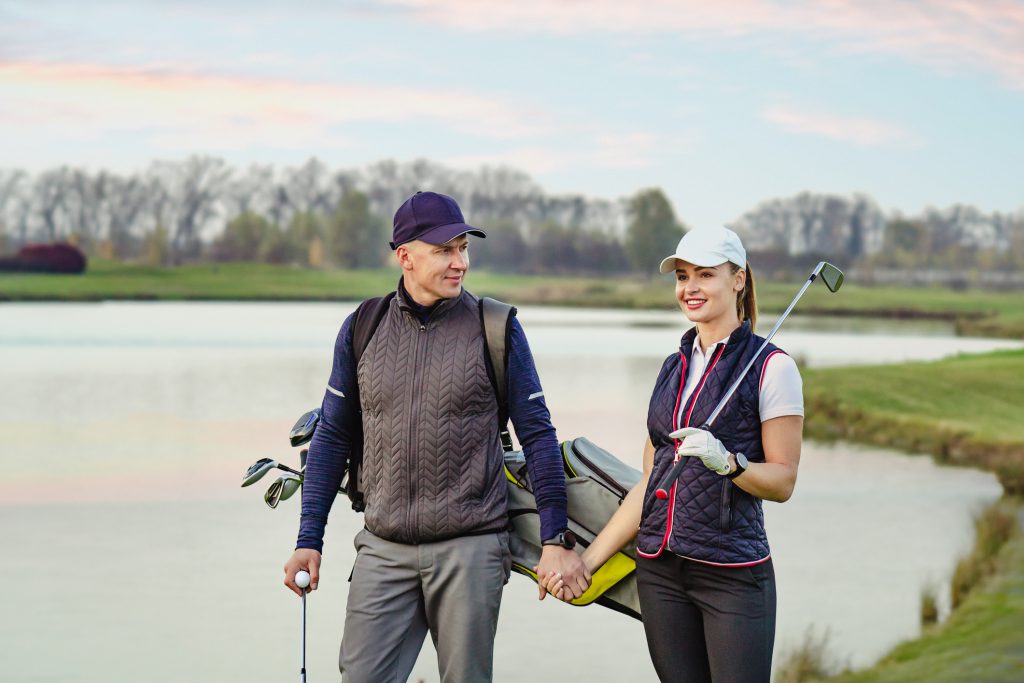 Portrait of sportive couple golfers playing golf at autumn day