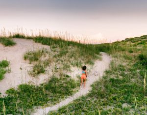 A child running along grassy sand dunes in the Outer Banks