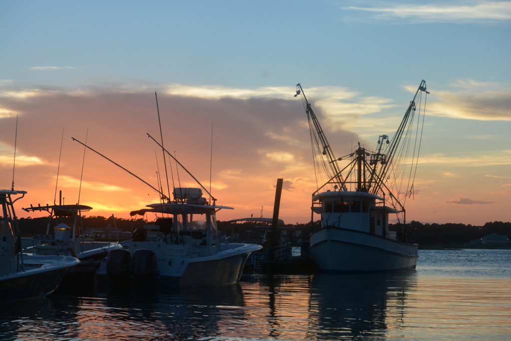 A marina / boat dock in Outer Banks, NC at sunset. The sun is setting on anchored fishing boats.