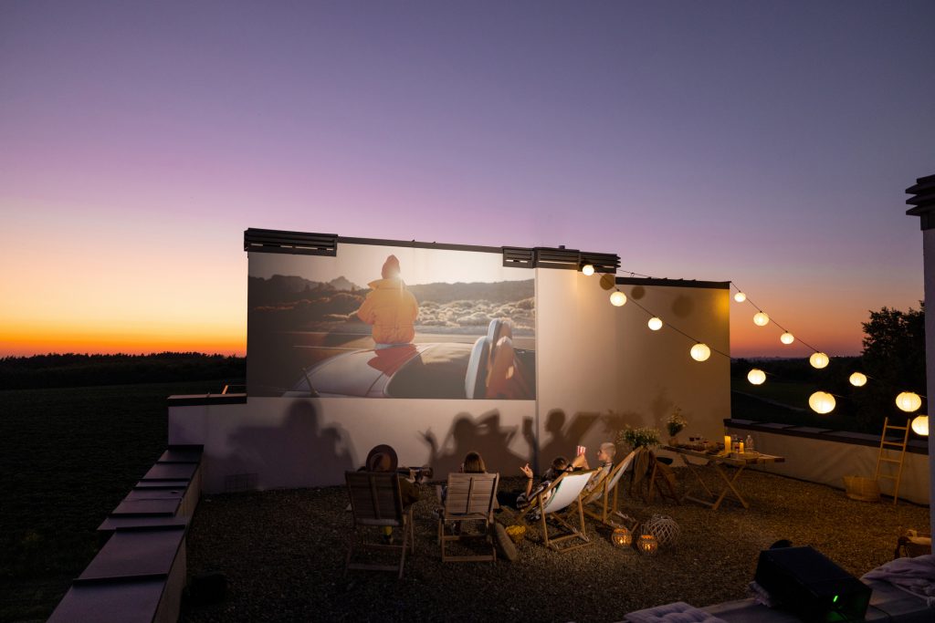 Small group of people watching movie outdoors at sunset. Open air cinema concept. 