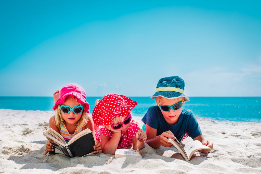 cute happy kids -boy and girls- read books on beach, family vacation concept