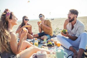 A group of young adults have a picnic on the beach during a sunny day