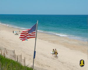 Overlook shot of a beach on the Outer Banks during the day with beachgoers and a flag waving in the wind along the sandy beach
