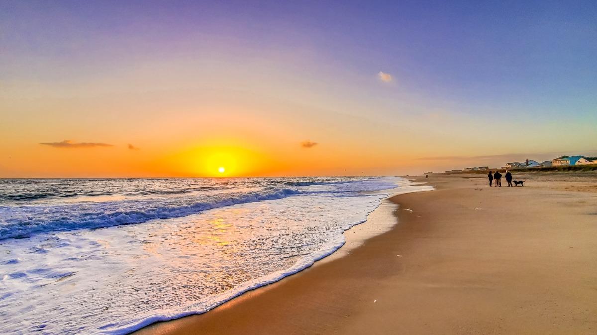 Sunset over the ocean with waves along the shore in the Outer Banks, perfect setting for families enjoying Outer Banks partial week rentals.